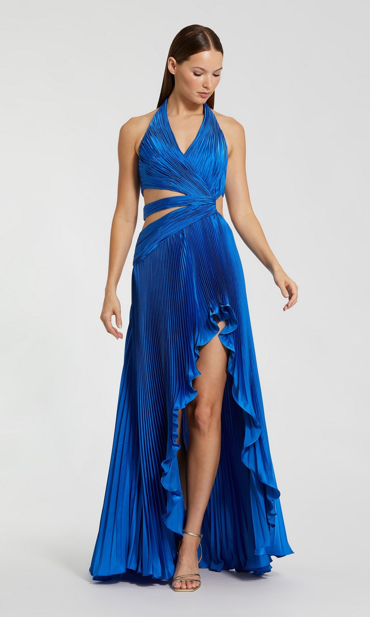 A woman wears the Long Formal Dress: Mac Duggal 49995, a sleeveless, halter-neck cobalt pleated charmeuse gown featuring cutout waist details and a high-low ruffled hem.